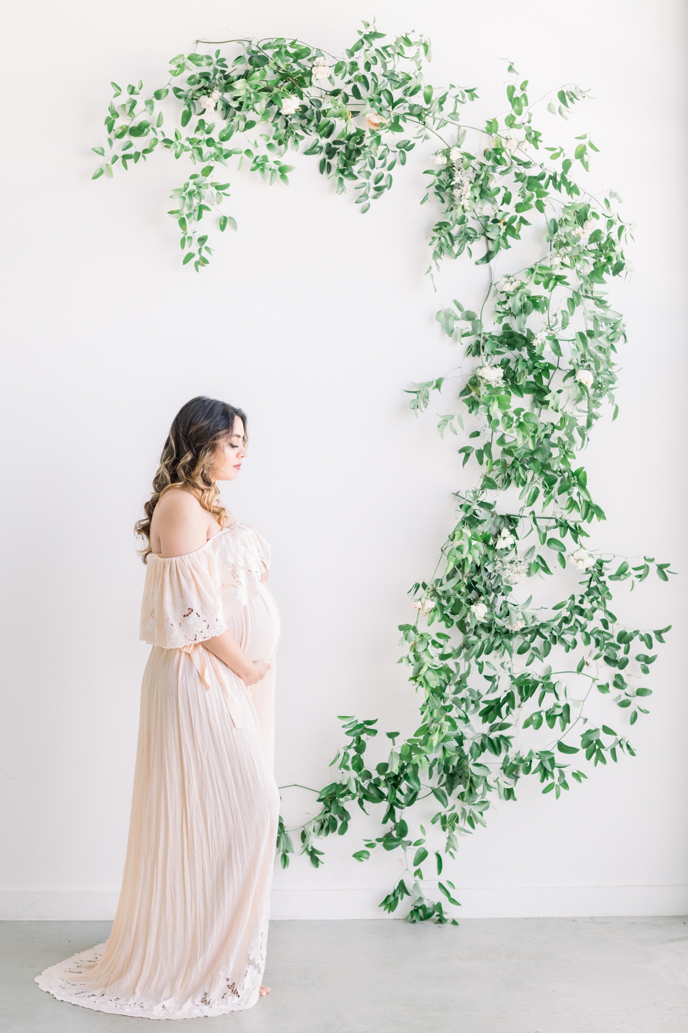 Mom in Fillyboo maxi dress during studio maternity session with florals in the background. Photo by Sana Ahmed Photography.