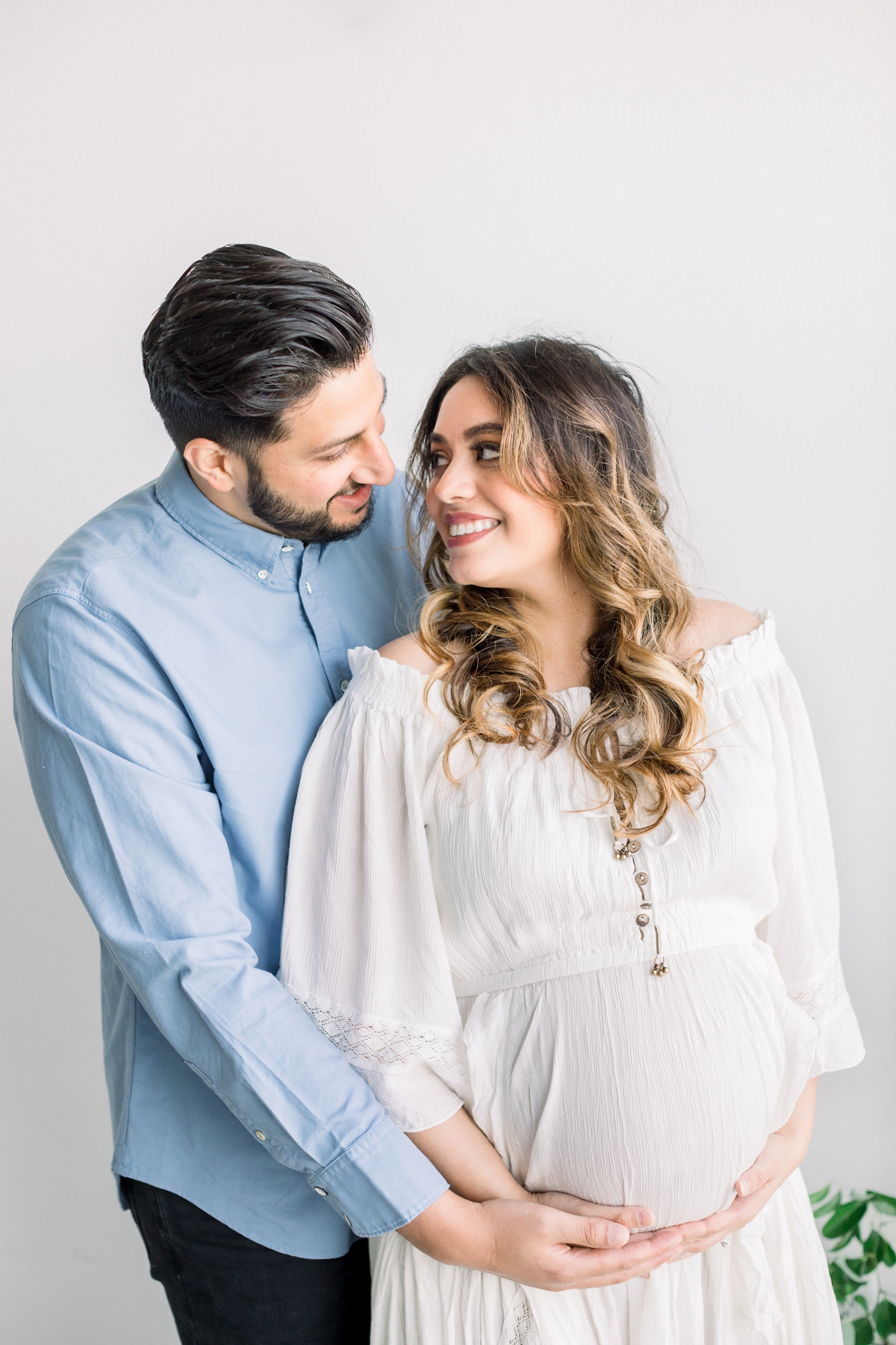 Mom and Dad smiling at each other in studio maternity session. Photo by Sana Ahmed Photography.