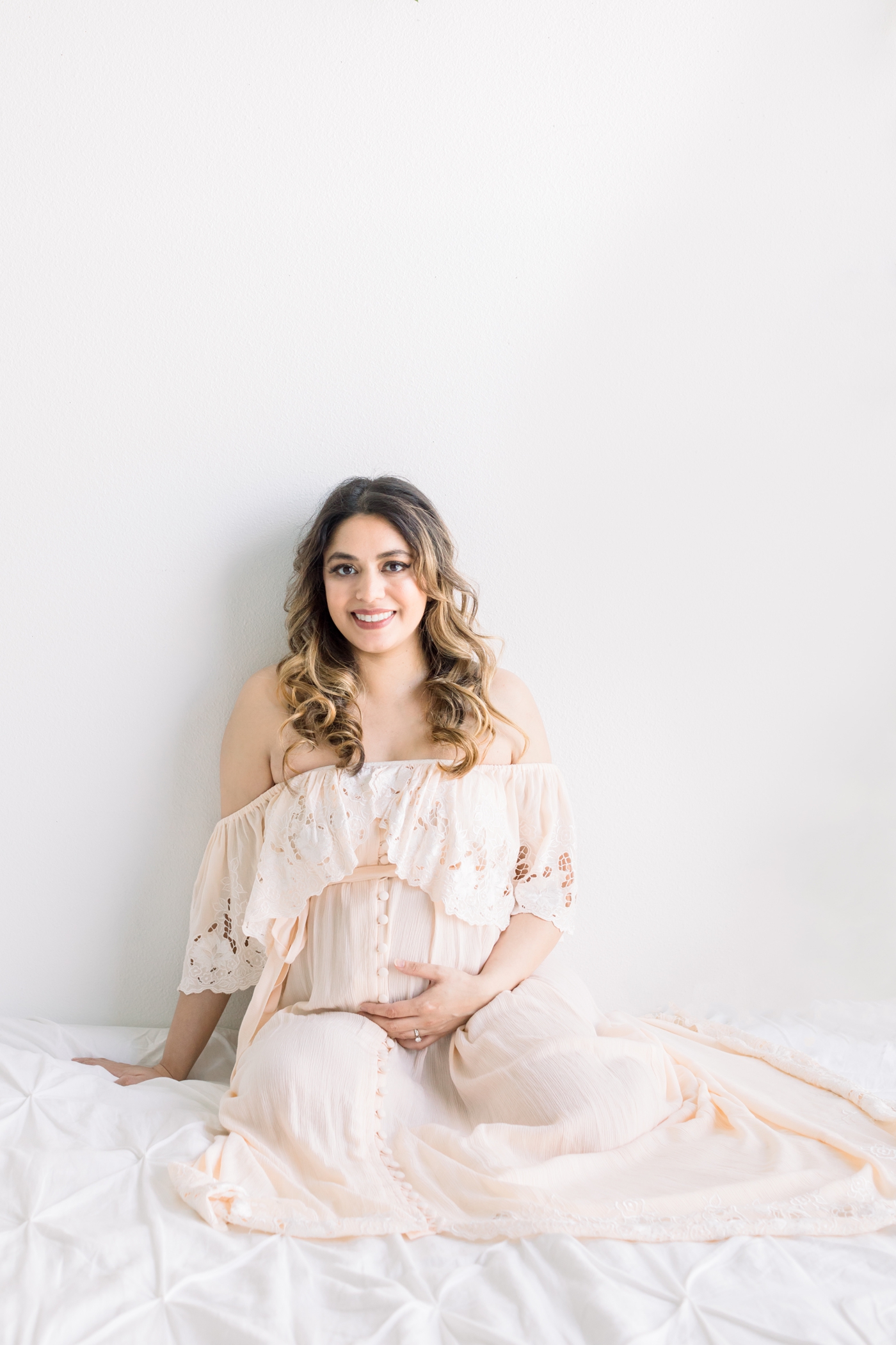 Mom wearing pink maternity maxi dress on bed during studio session with Austin Maternity Photographer, Sana Ahmed Photography.