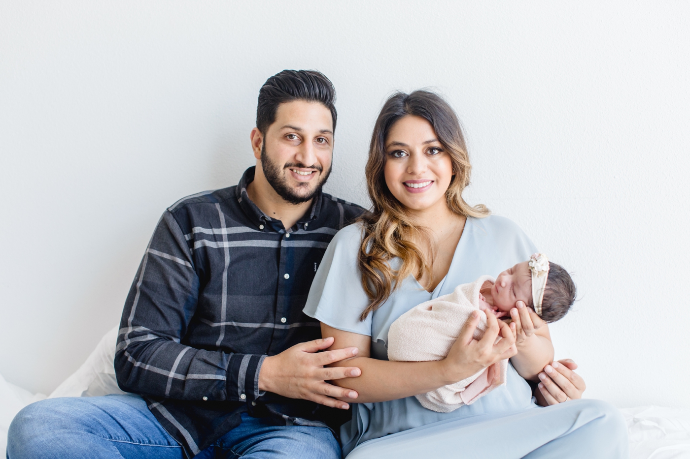 Parents smiling at the camera on bed in studio. Photo by Austin Newborn Photographer, Sana Ahmed Photography