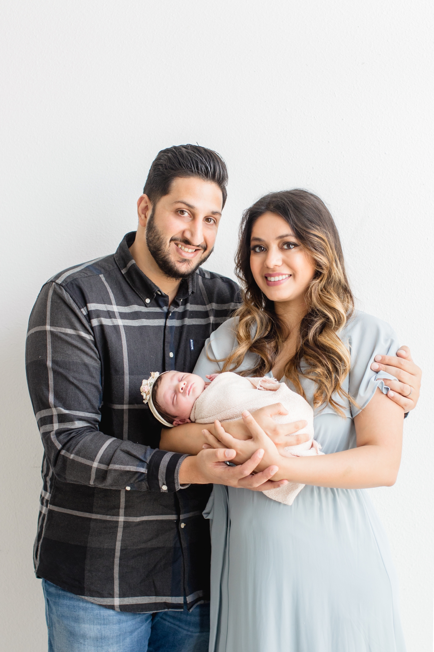 Mom and Dad smiling at camera while holding baby girl during studio newborn session in Austin, TX. Photo by Sana Ahmed Photography