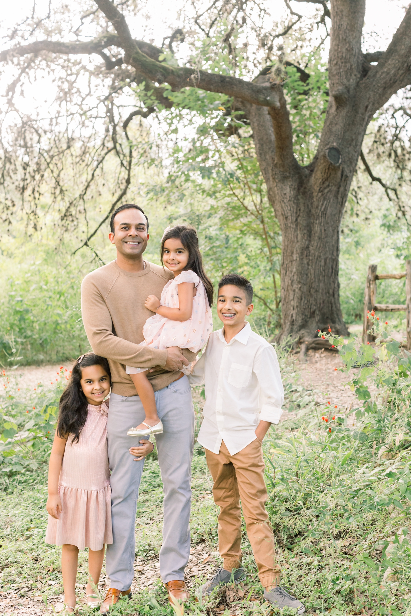 Dad with three children under oak trees in Austin, TX. Photo by Sana Ahmed Photography.