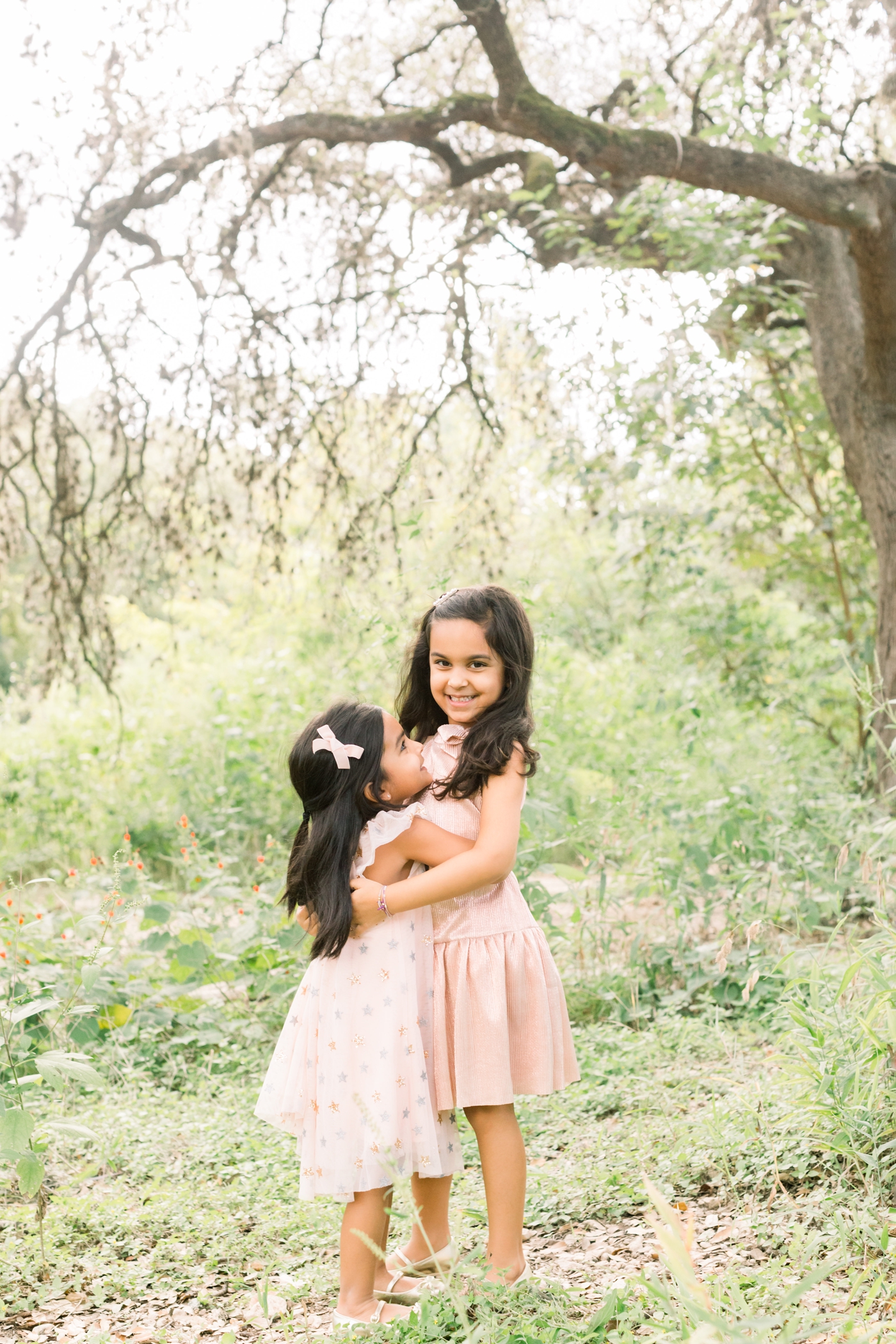 Sisters hugging during family session in field near Austin TX. Photo by Sana Ahmed Photography.