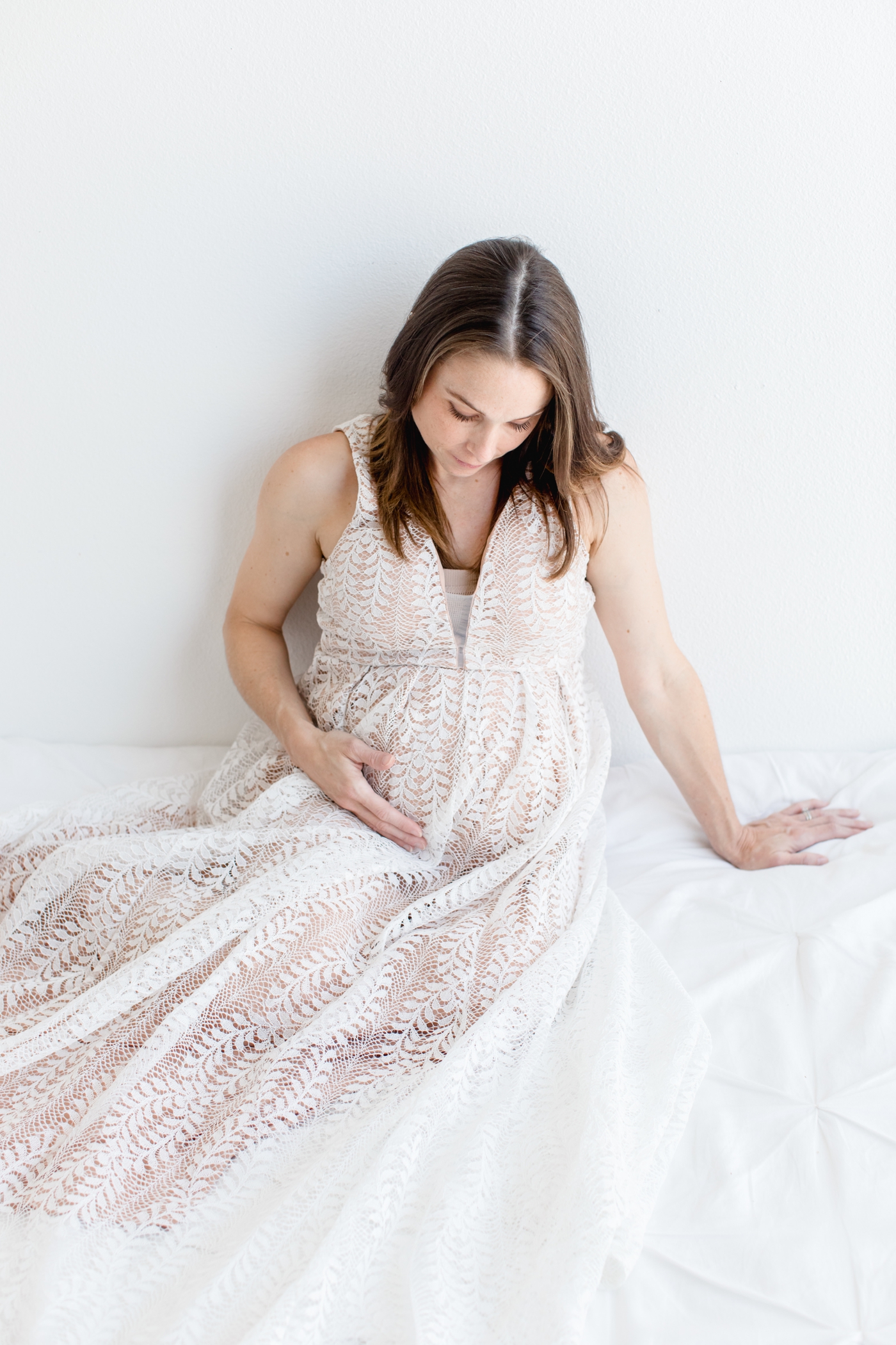 Beautiful expecting Mom leaning on bed and looking at her bump. Photo by Austin TX maternity photographer, Sana Ahmed Photography.