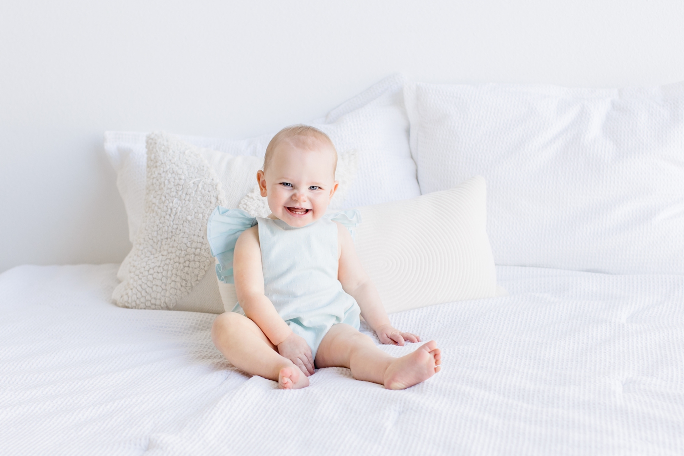 Toddler with big smile sitting on bed during studio session. Photo by Sana Ahmed Photography.