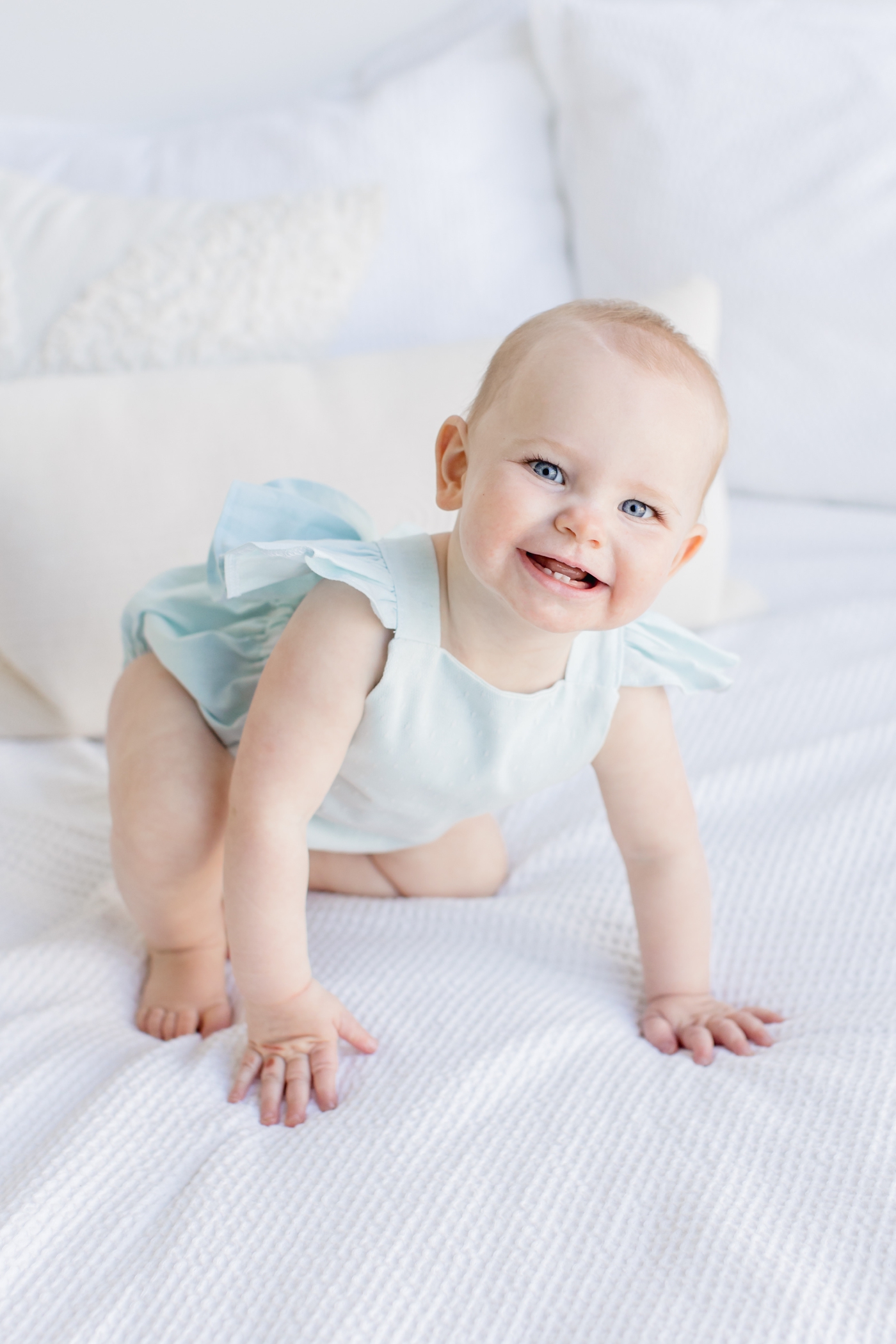 Toddler with a big smile while crawling on the bed in studio session. Photo by Austin family photographer, Sana Ahmed Photography.