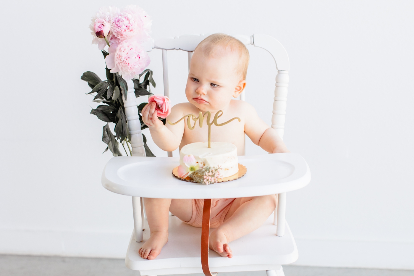 Toddler looking at flower from her cake during her first birthday milestone session. Photo by Sana Ahmed Photography.