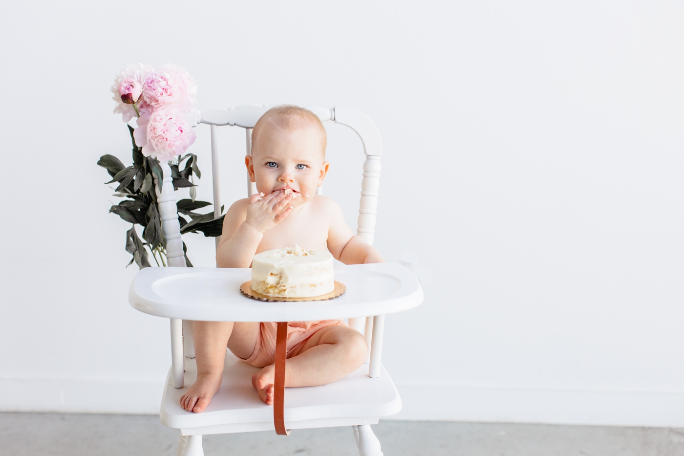 Little girl tasting frosting during her cake smash in studio by Sana Ahmed Photography.