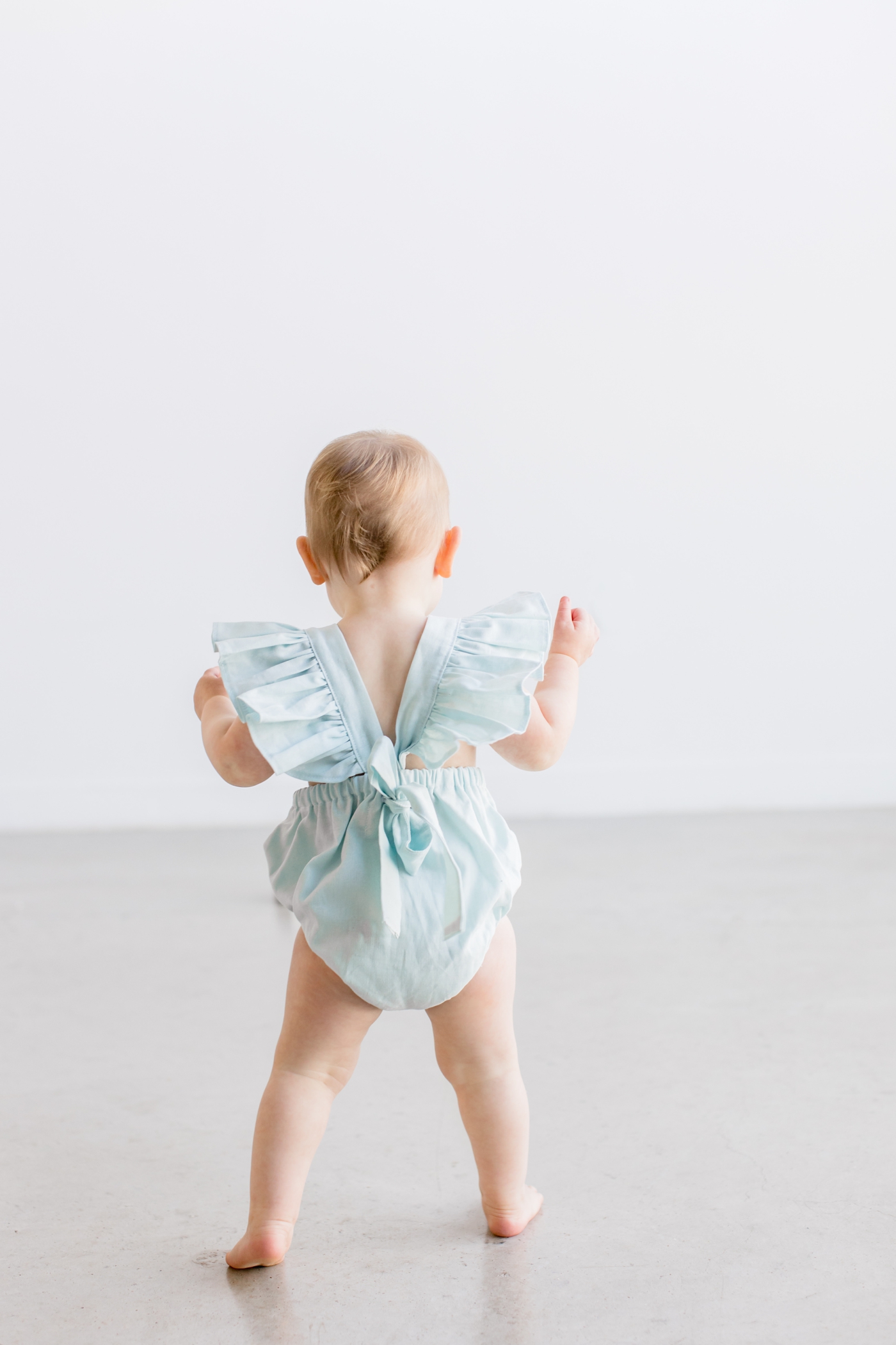 Toddler walking in adorable romper with flutter sleeves during milestone session by Sana Ahmed Photography.