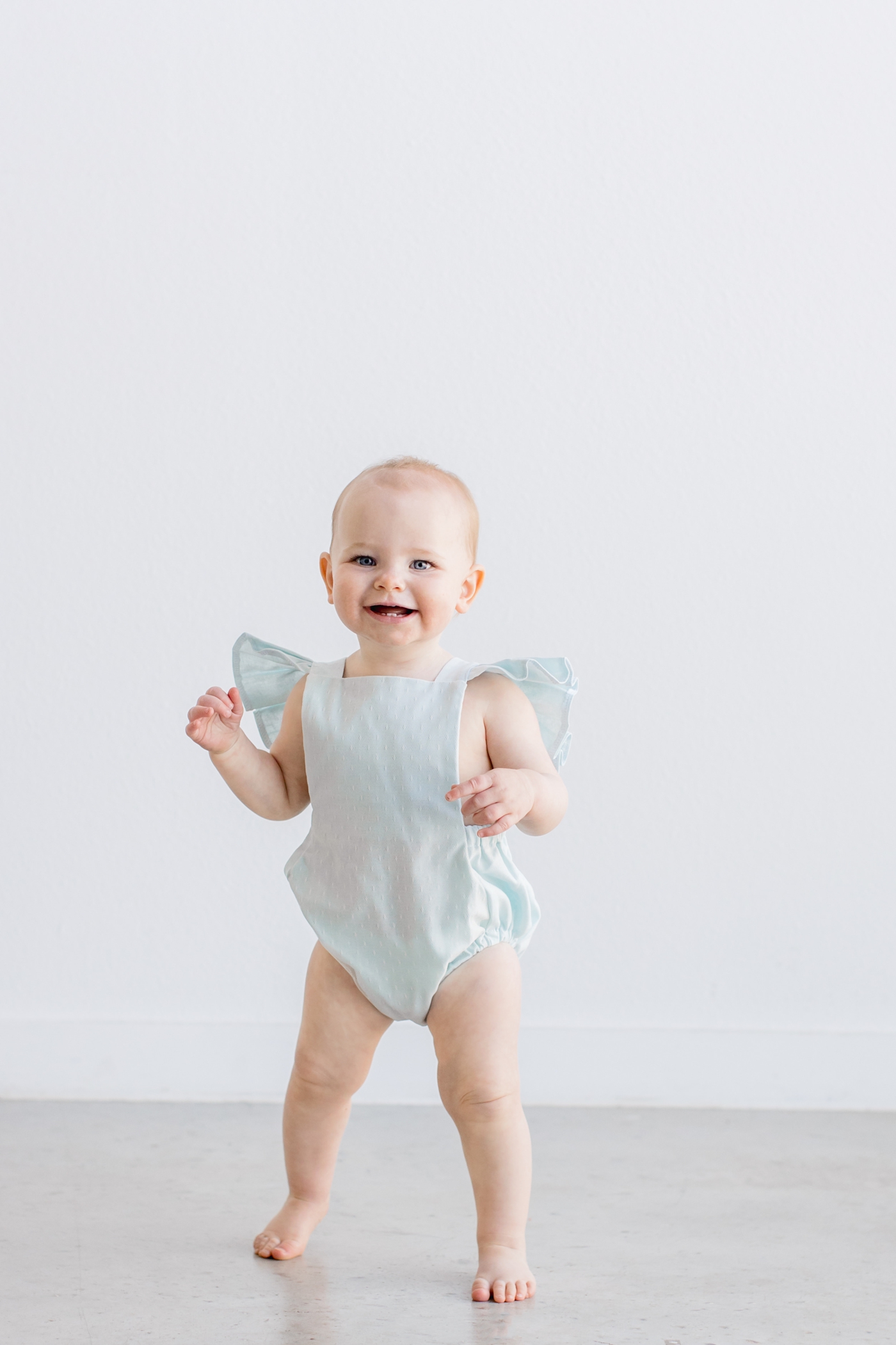 Toddler smiling and walking in studio milestone session. Photo by Sana Ahmed Photography.