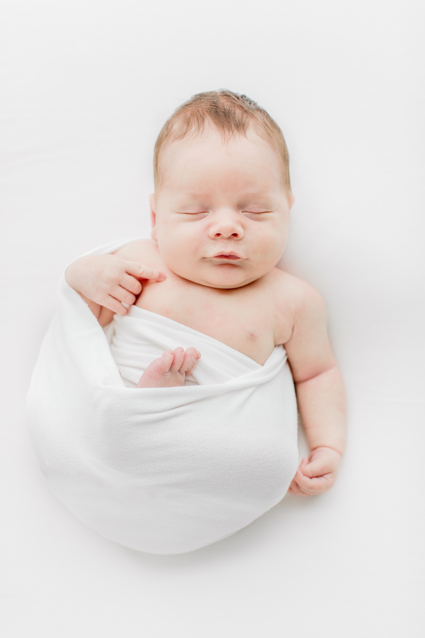 Baby boy sleeping in white swaddle during studio newborn session. Photo by Sana Ahmed Photography.
