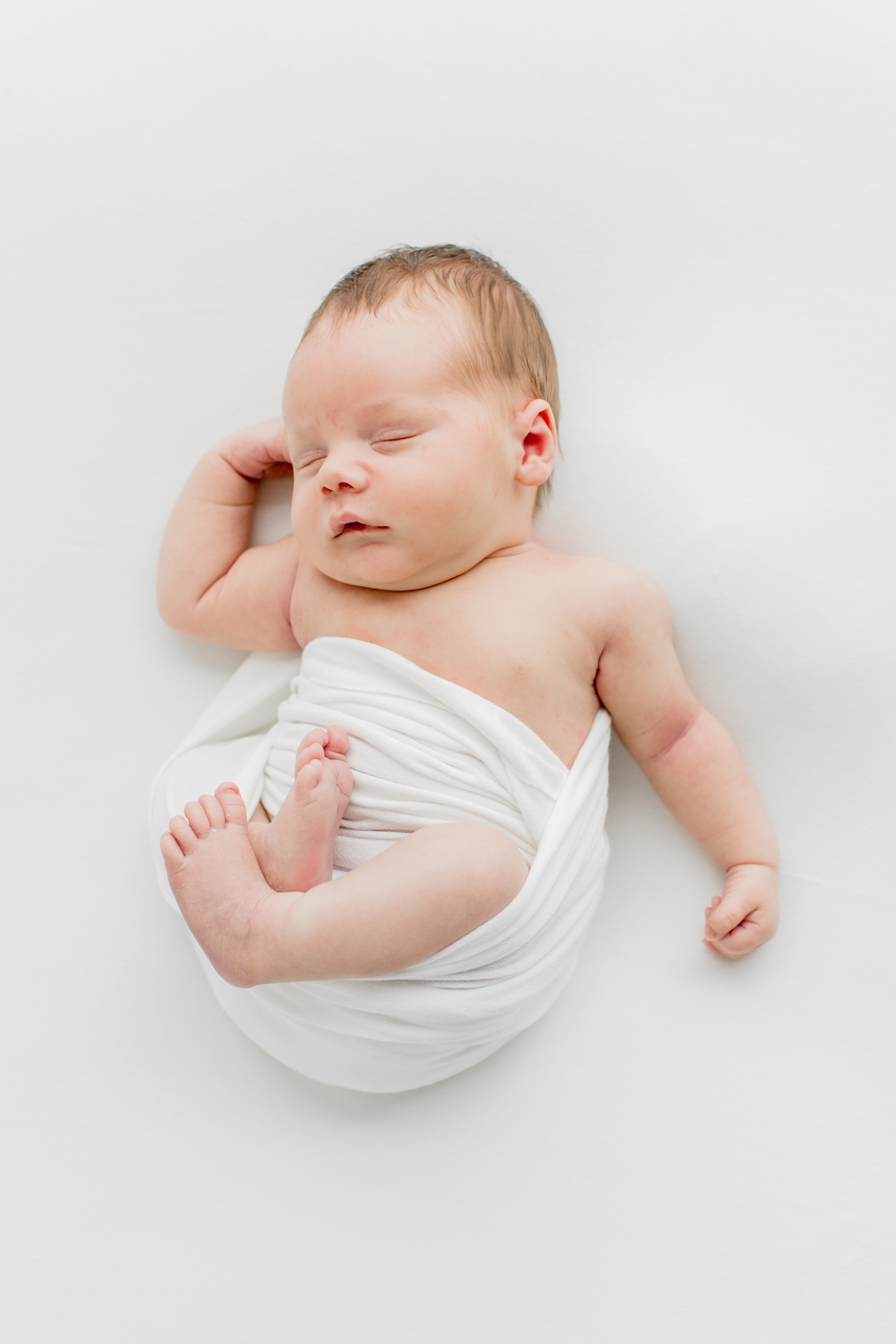 Baby boy sleeping in white swaddle during newborn session in Austin, TX studio. Photo by Sana Ahmed Photography.