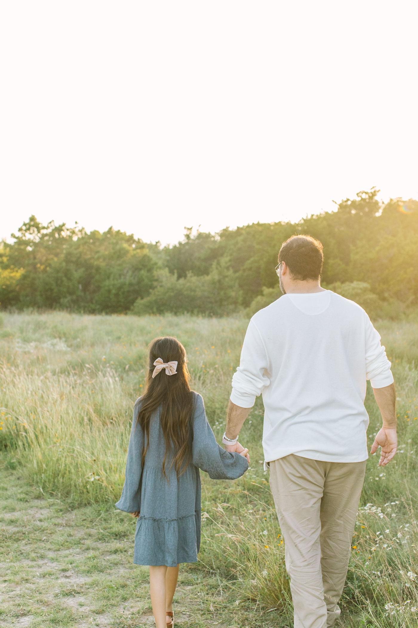 Dad holding daughter's hand and walking in field during family session in Austin, TX. Photo by Sana Ahmed Photography.