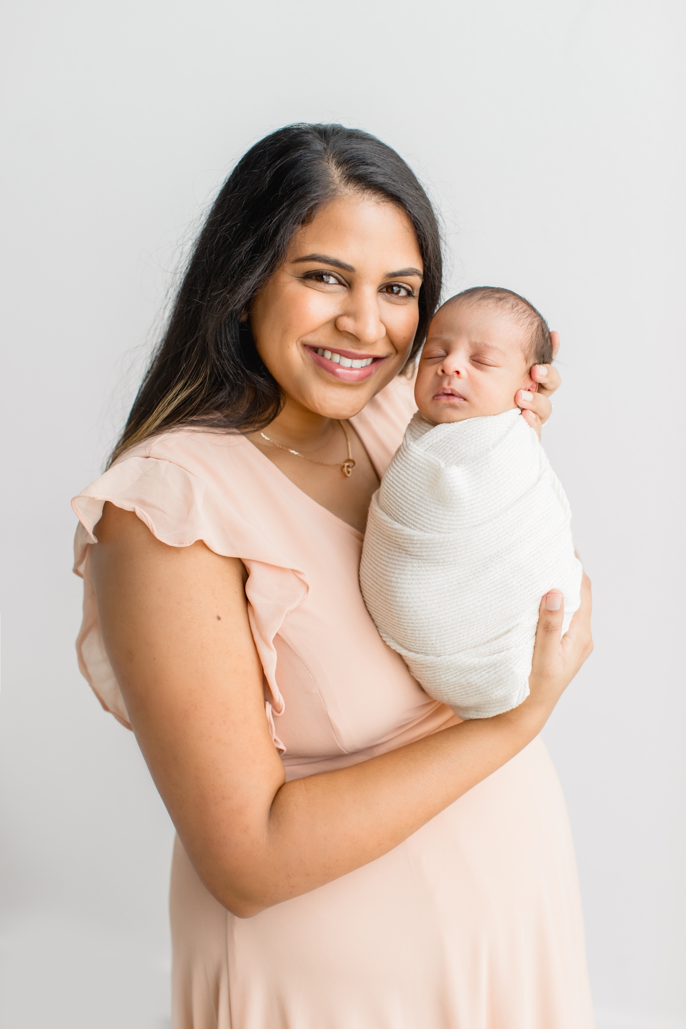 Mom holding baby wrapped in white swaddle during newborn session by Austin TX baby photographer, Sana Ahmed Photography.