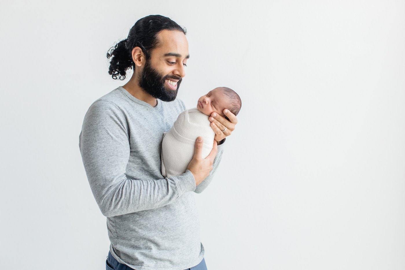 Dad smiling at baby wrapped in white knit swaddle. Photo by Sana Ahmed Photography.