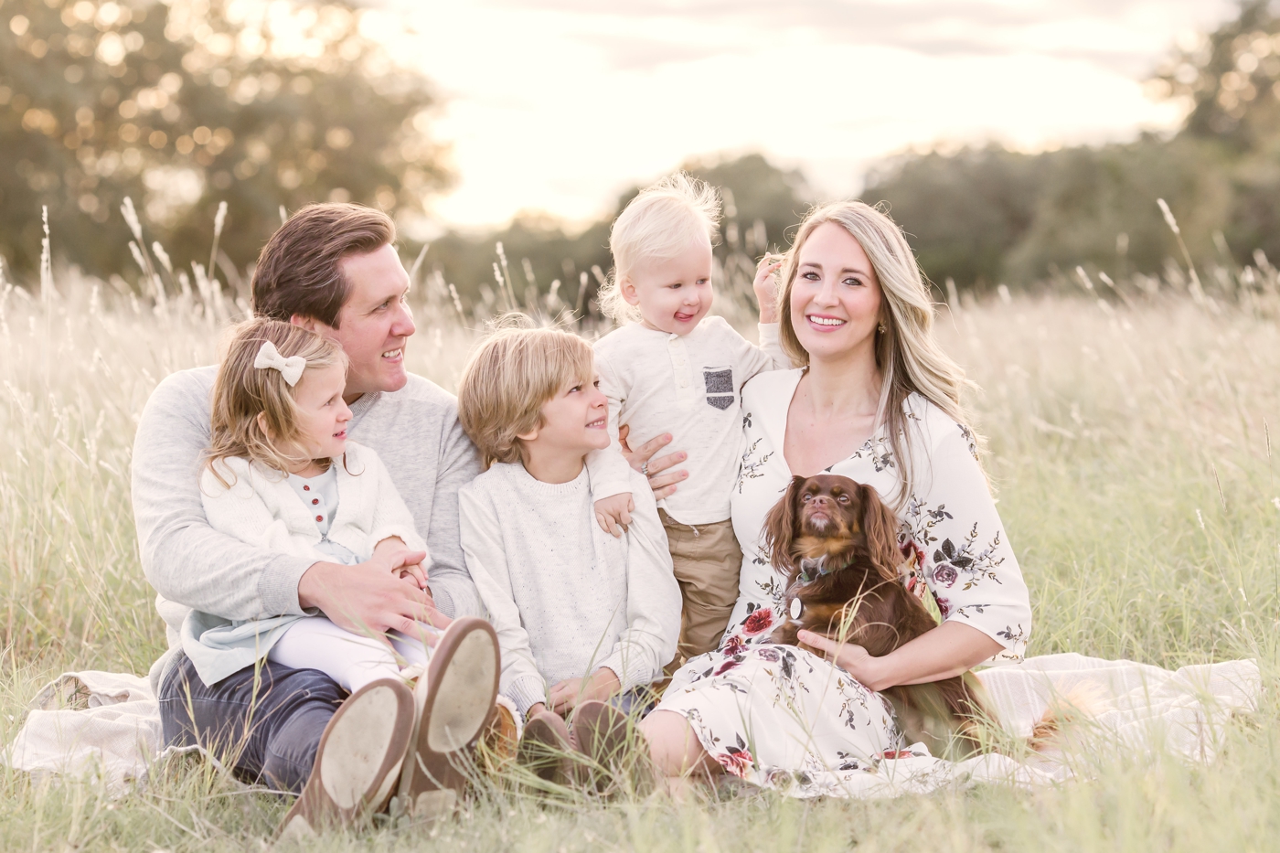 Family of five with dog cuddling in tall grass. Photo by Austin Family Photographer, Sana Ahmed Photography.