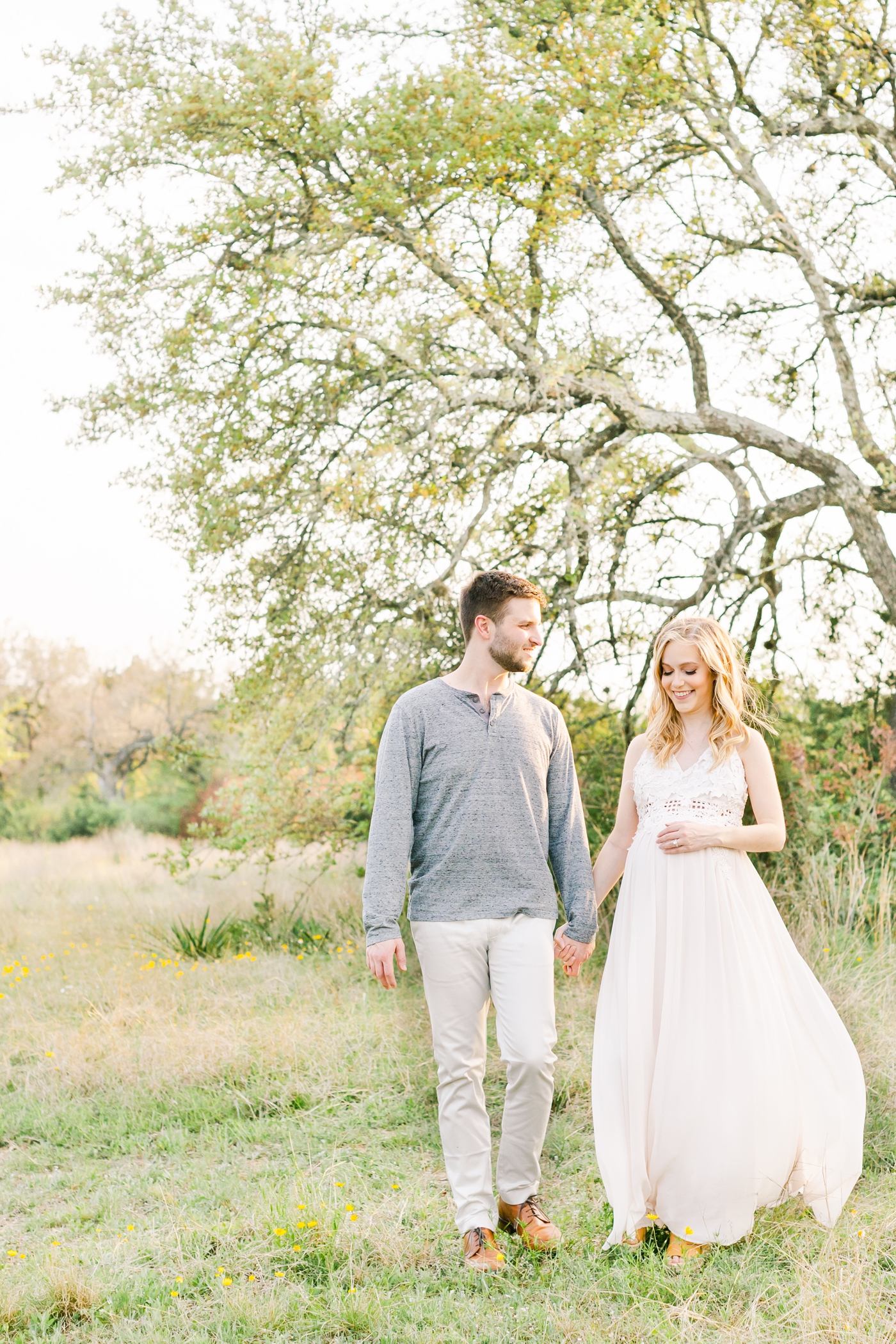 Expecting parents holding hands and walking in field of wildflowers. Photo by Austin maternity photographer, Sana Ahmed Photography.