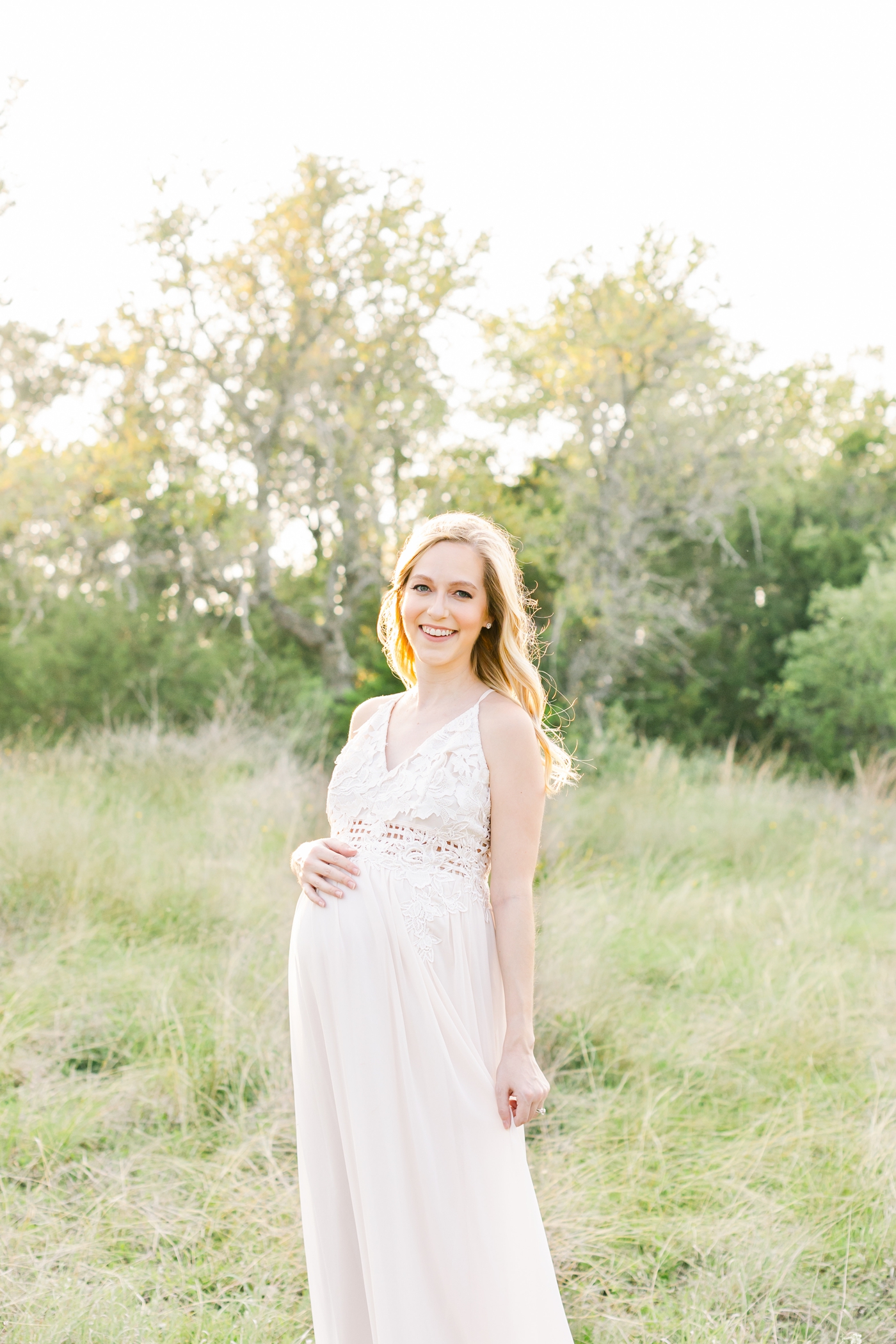 Mom wearing white maxi dress with lace during maternity session in field with tall grass. Photo by Sana Ahmed Photography.