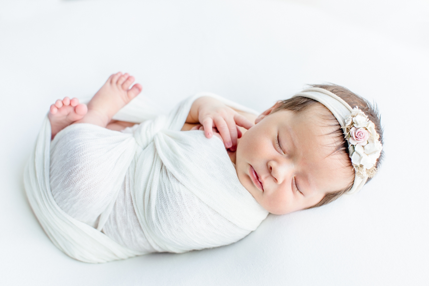 Side angle of sleeping baby girl in white swaddle with floral headband on her hair. Photo by Sana Ahmed Photography.