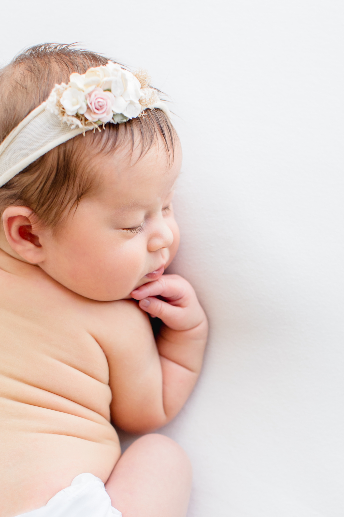 Closeup of baby girl with newborn rolls and floral headband during studio session. Photo by Austin TX baby photographer, Sana Ahmed Photography.