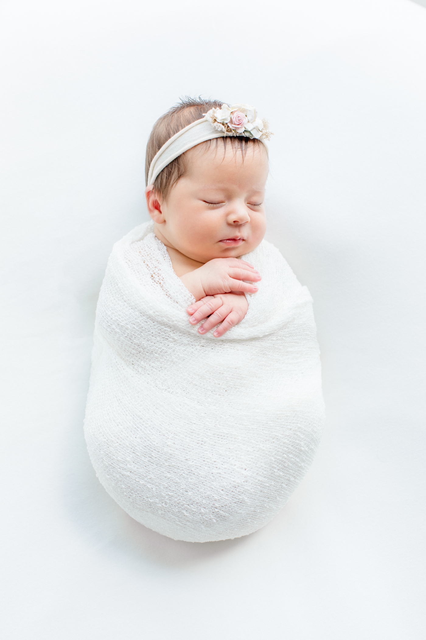 Sleeping baby girl in white swaddle on white backdrop. Photo by Sana Ahmed Photography.