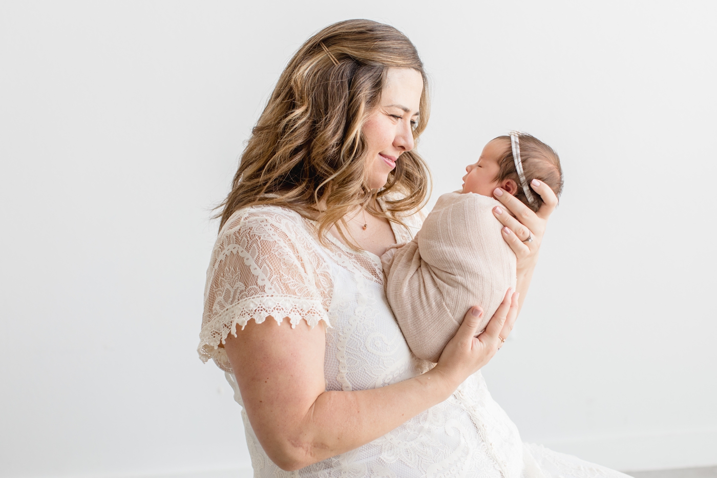 Mom holding baby girl up close and smiling at her. during studio newborn session. Photo by Sana Ahmed Photography.
