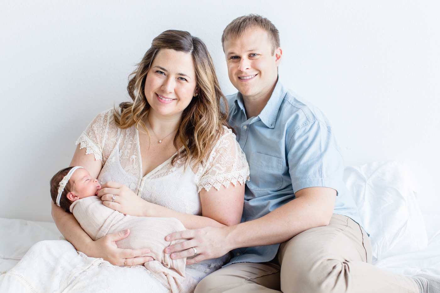 New parents sitting on bed while holding baby. Photo by Sana Ahmed Photography.