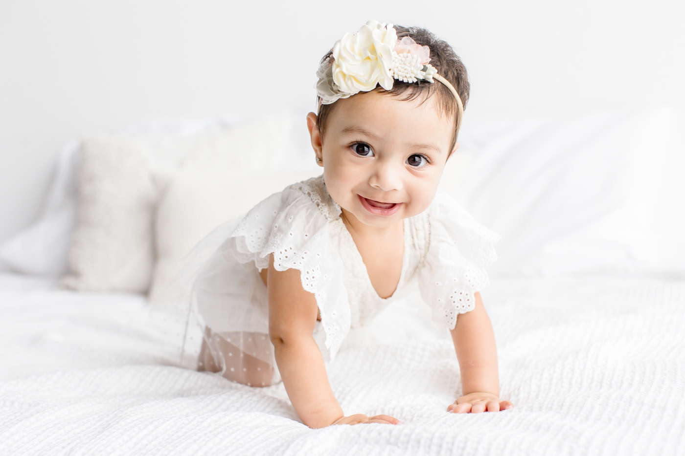 Baby girl smiling at camera and crawling on bed during 6 month milestone session. Photo by Sana Ahmed Photography.