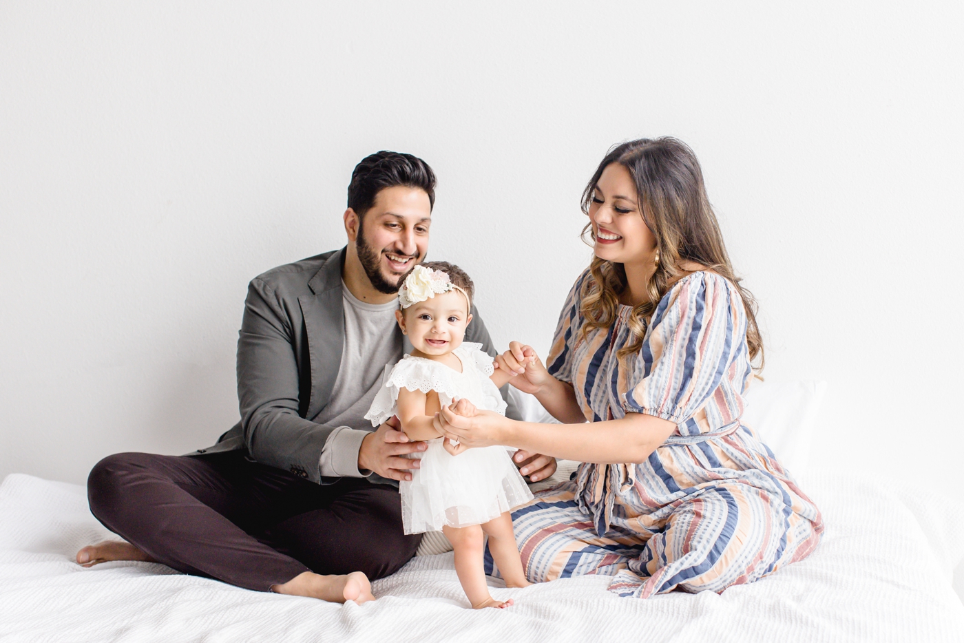 Baby girl smiling with parents during milestone photoshoot in studio. Photo by Cedar Park family photographer, Sana Ahmed Photography.