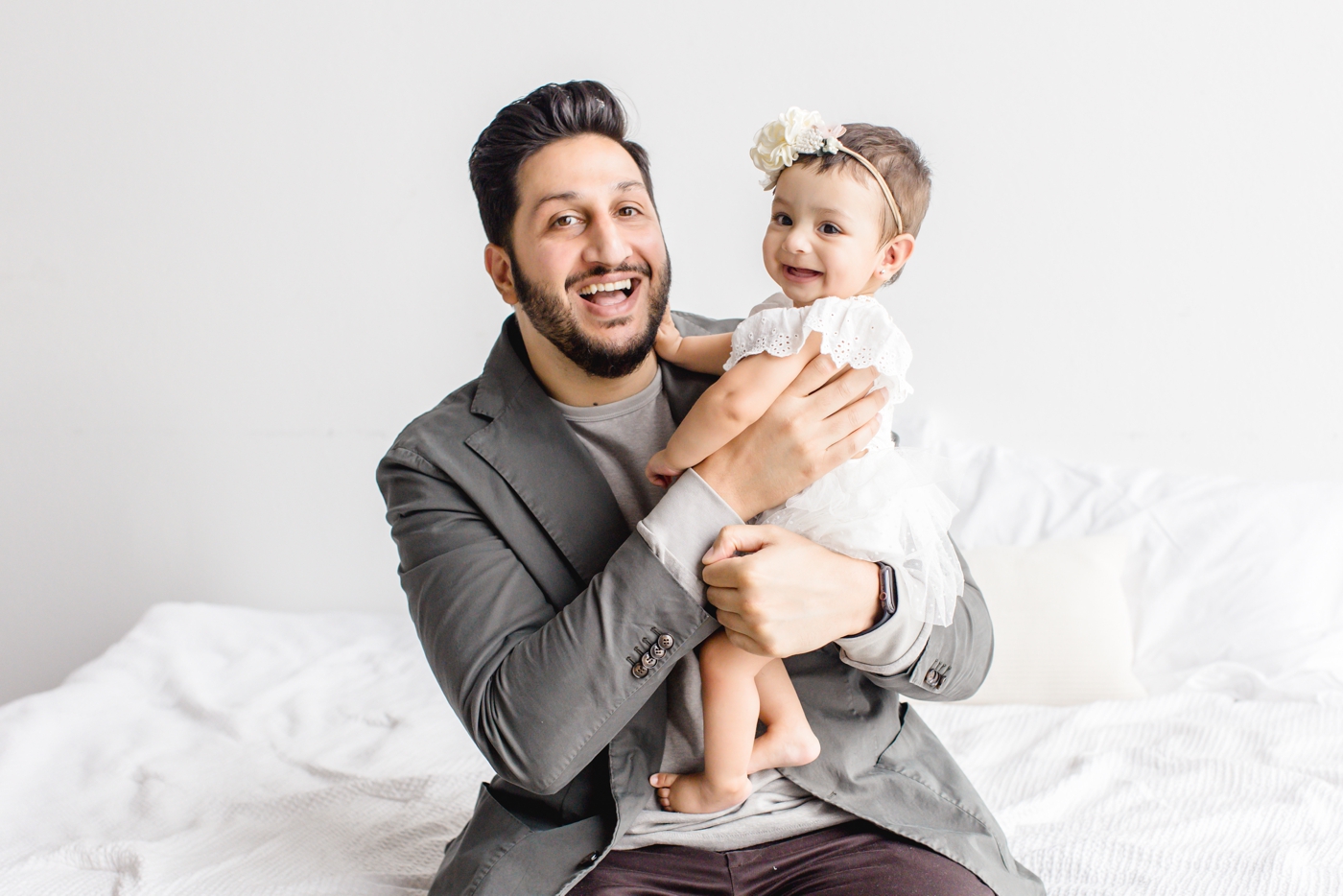 Dad and baby girl smiling at camera during studio session in Cedar Park, TX. Photo by Sana Ahmed Photography.