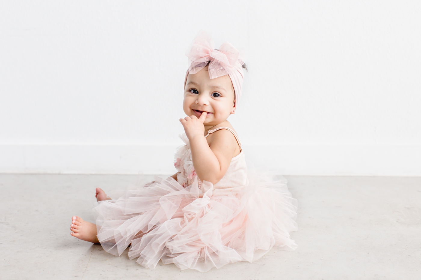 Baby girl smiling at camera while wearing light pink tulle dress for milestone session. Photo by Sana Ahmed Photography.