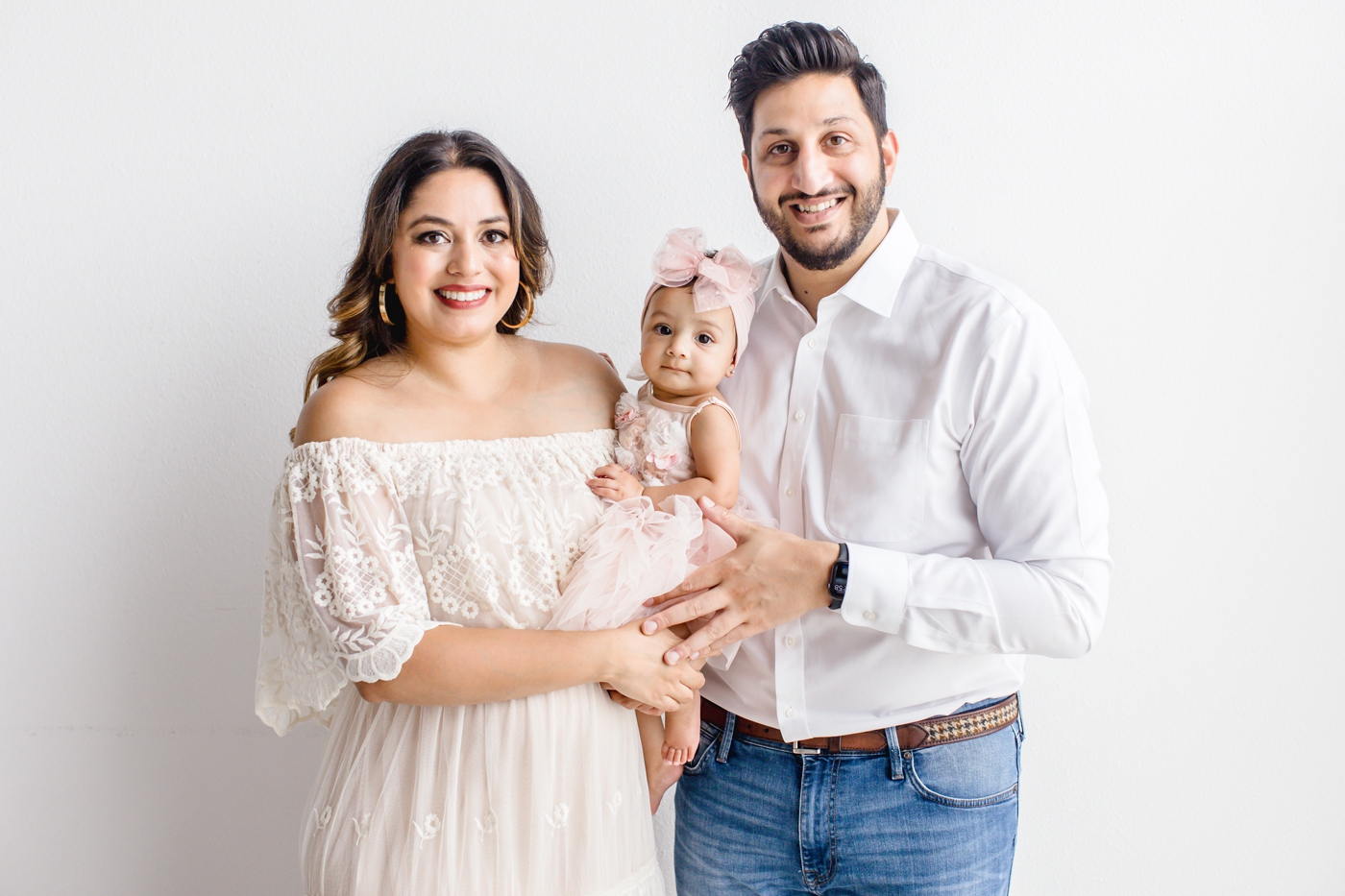 Mom, Dad and baby smiling at camera during studio family session. Photo by Sana Ahmed Photography.