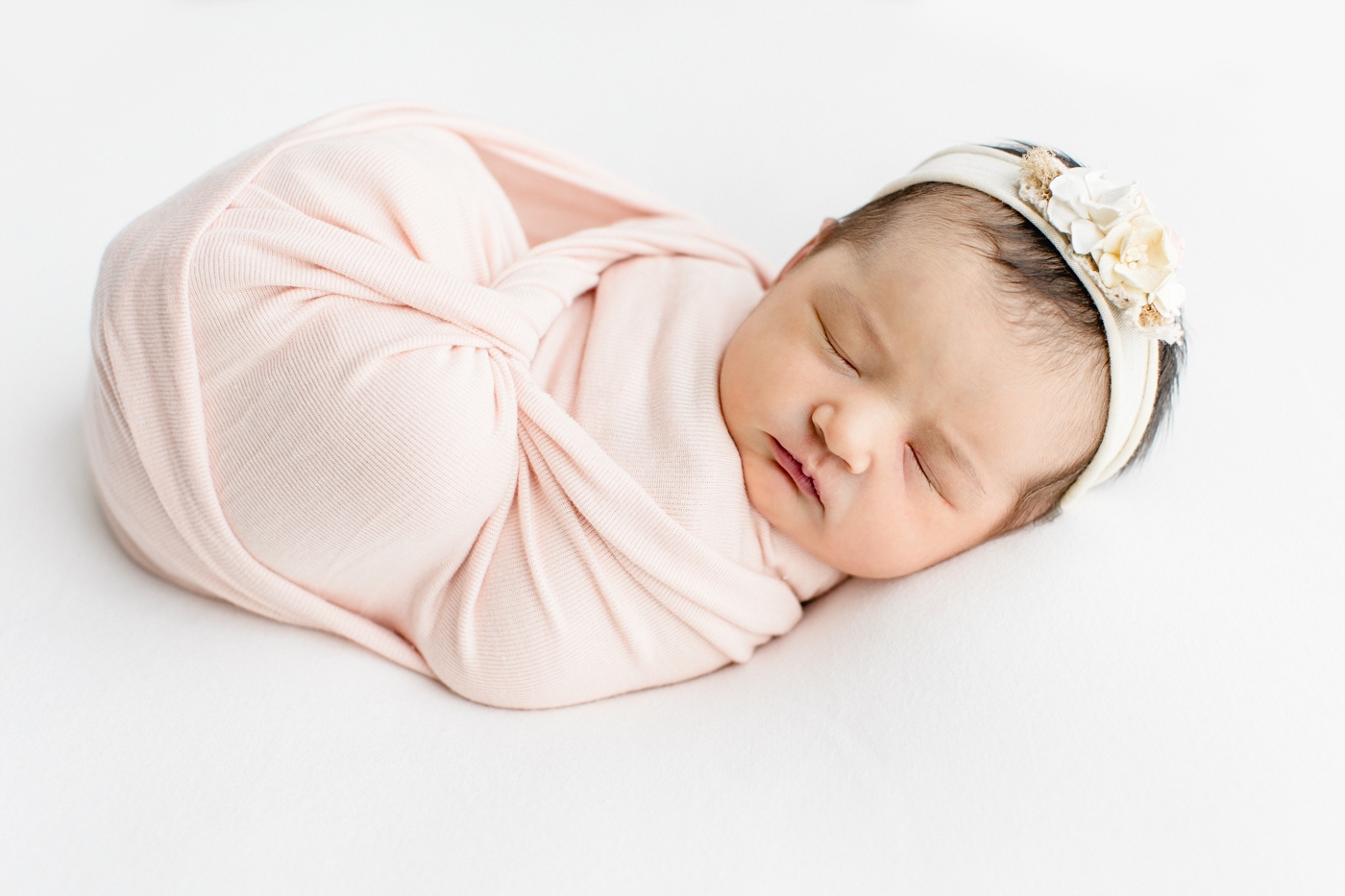Baby in light pink swaddle with floral headband. Photo by Sana Ahmed Photography.