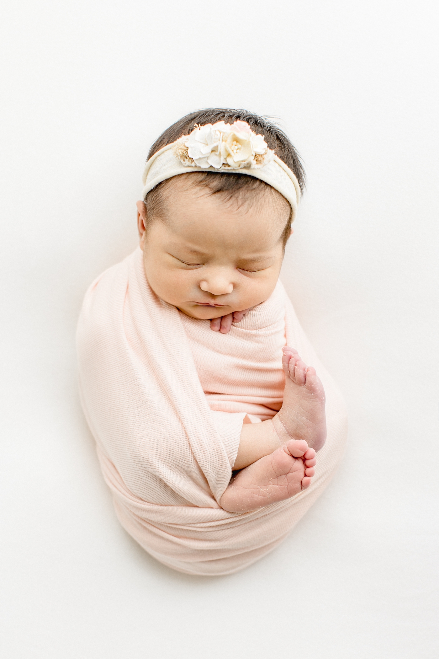 Baby girl in light pink swaddle with floral headband. Photo by Cedar Park newborn photographer, Sana Ahmed Photography.