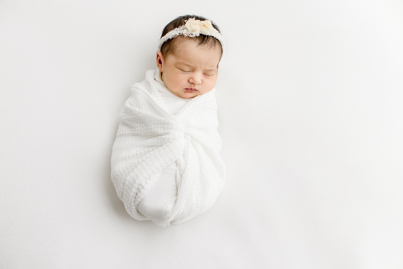Baby wrapped in white knit swaddle and sleeping during studio newborn session in Cedar Park TX.Photo by Sana Ahmed Photography.