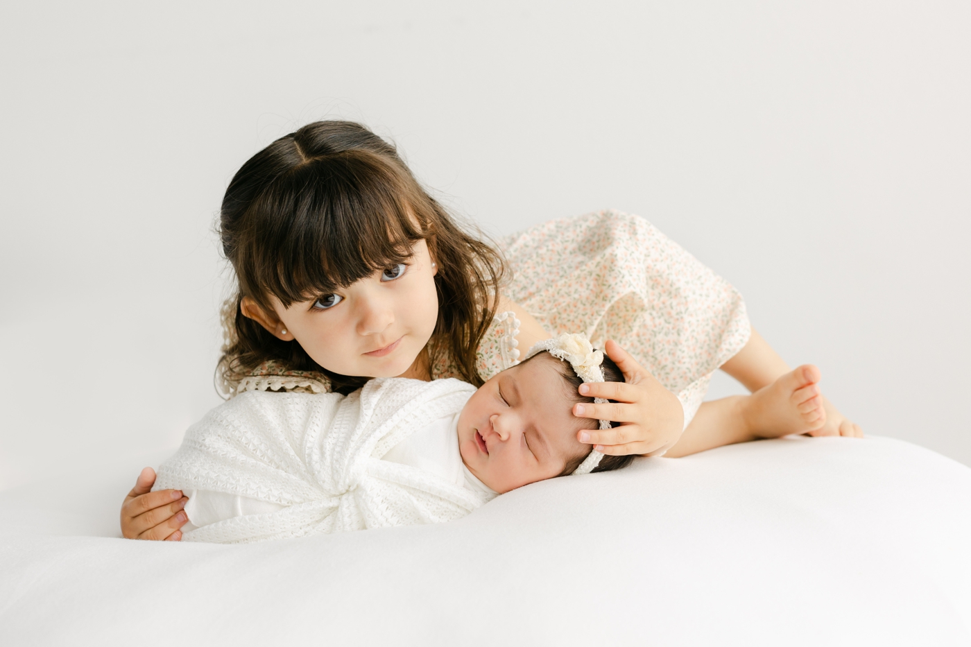 Big sister hugging baby in white swaddle during Cedar Park studio newborn session. Photo by Sana Ahmed Photography.
