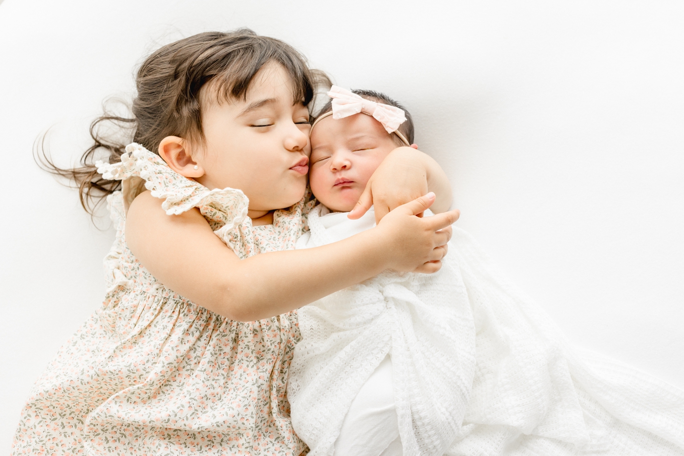Big sister holding and kissing baby sister. Photo by Cedar park newborn photographer,Sana Ahmed Photography.