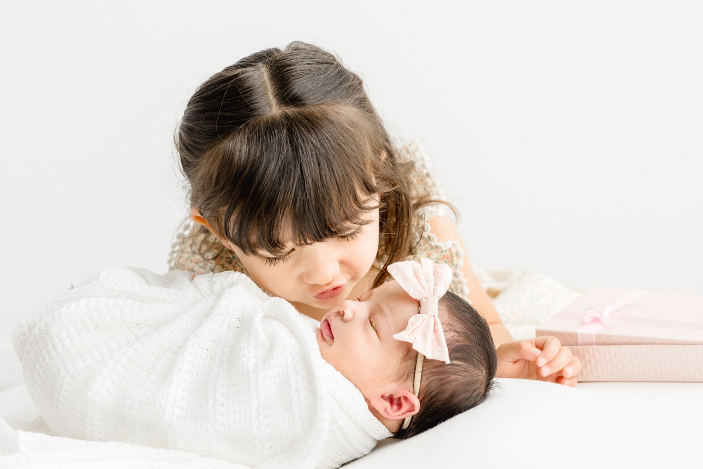 Big sister kissing baby sister during studio newborn session. Photo by Cedar Park newborn photographer, Sana Ahmed Photography.