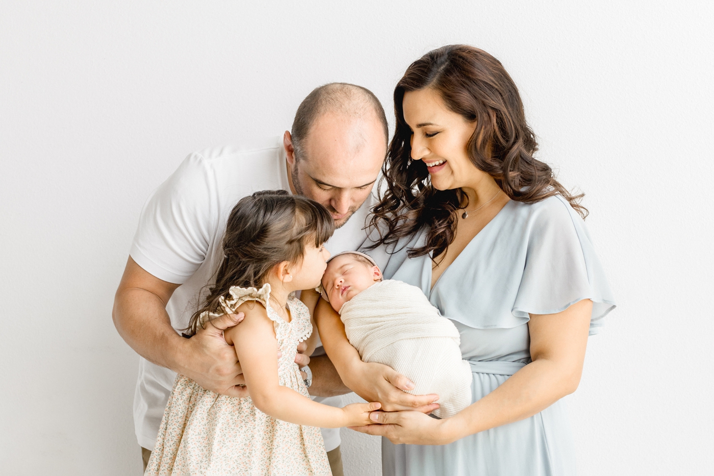 Family of four portrait with big sister kissing baby sister. Photo by Cedar Park newborn photographer, Sana Ahmed Photography.