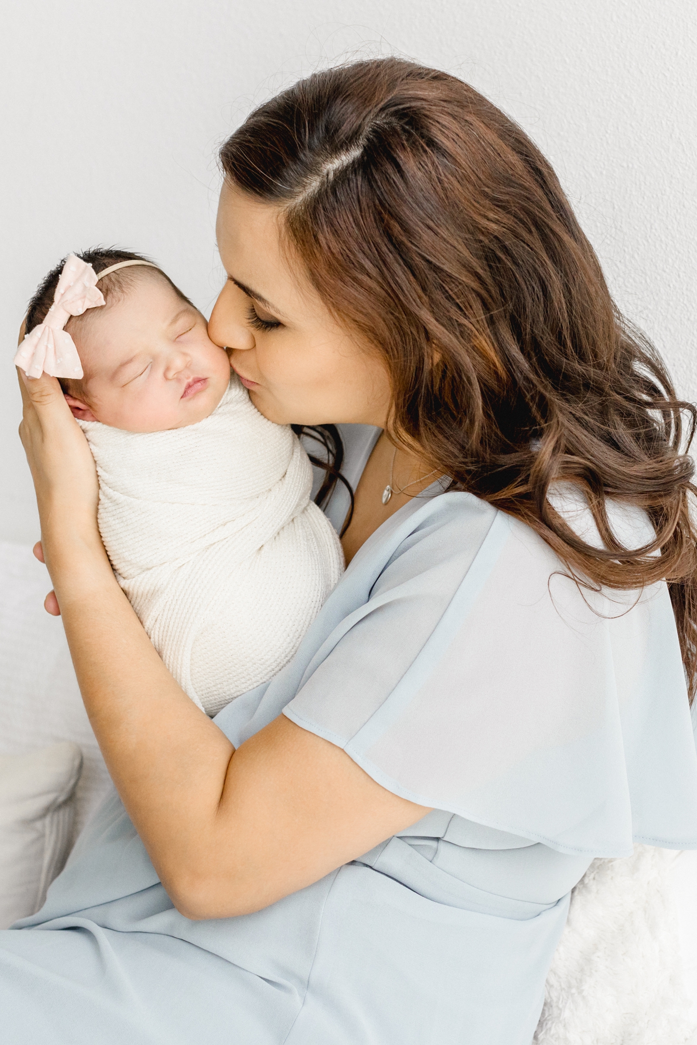 Mom kissing baby while she sleeps in white swaddle. Photo by Cedar Park newborn photographer, Sana Ahmed Photography.