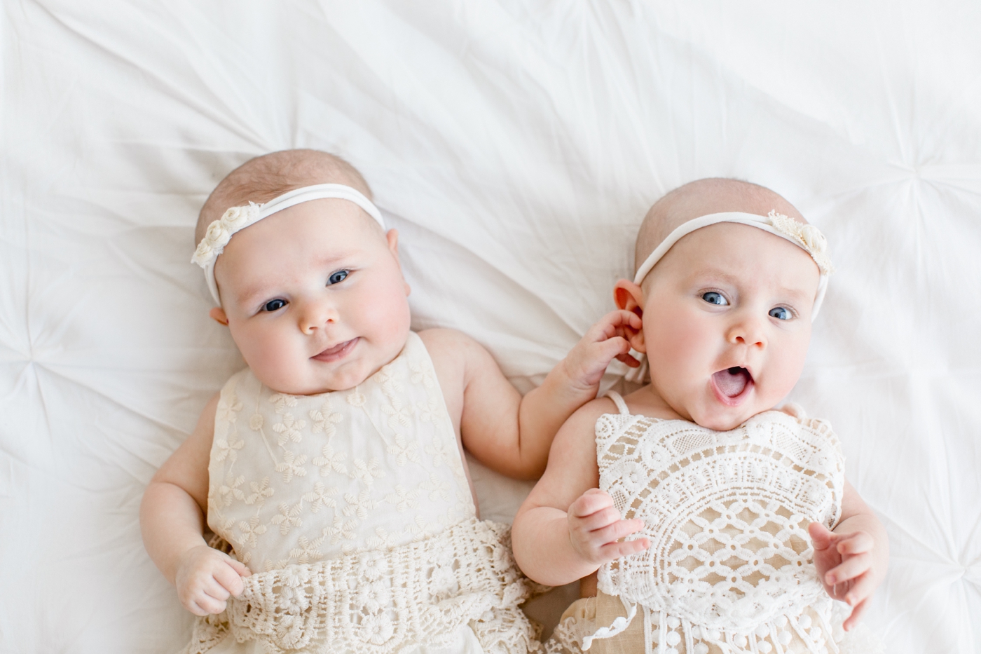 Twin baby girls laying next to each other on bed in studio. Photo by Sana Ahmed Photography.