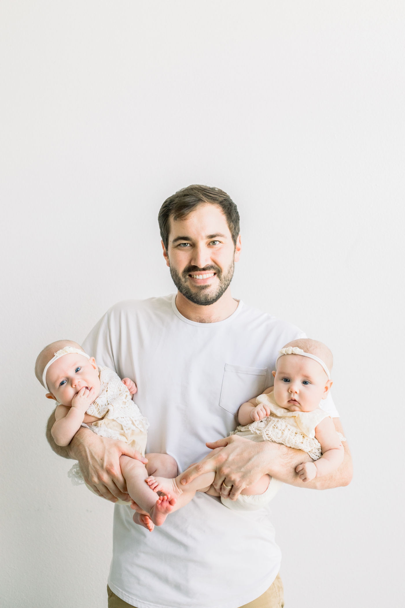 Dad holding twin daughters and smiling at camera. Photo by Sana Ahmed Photography.