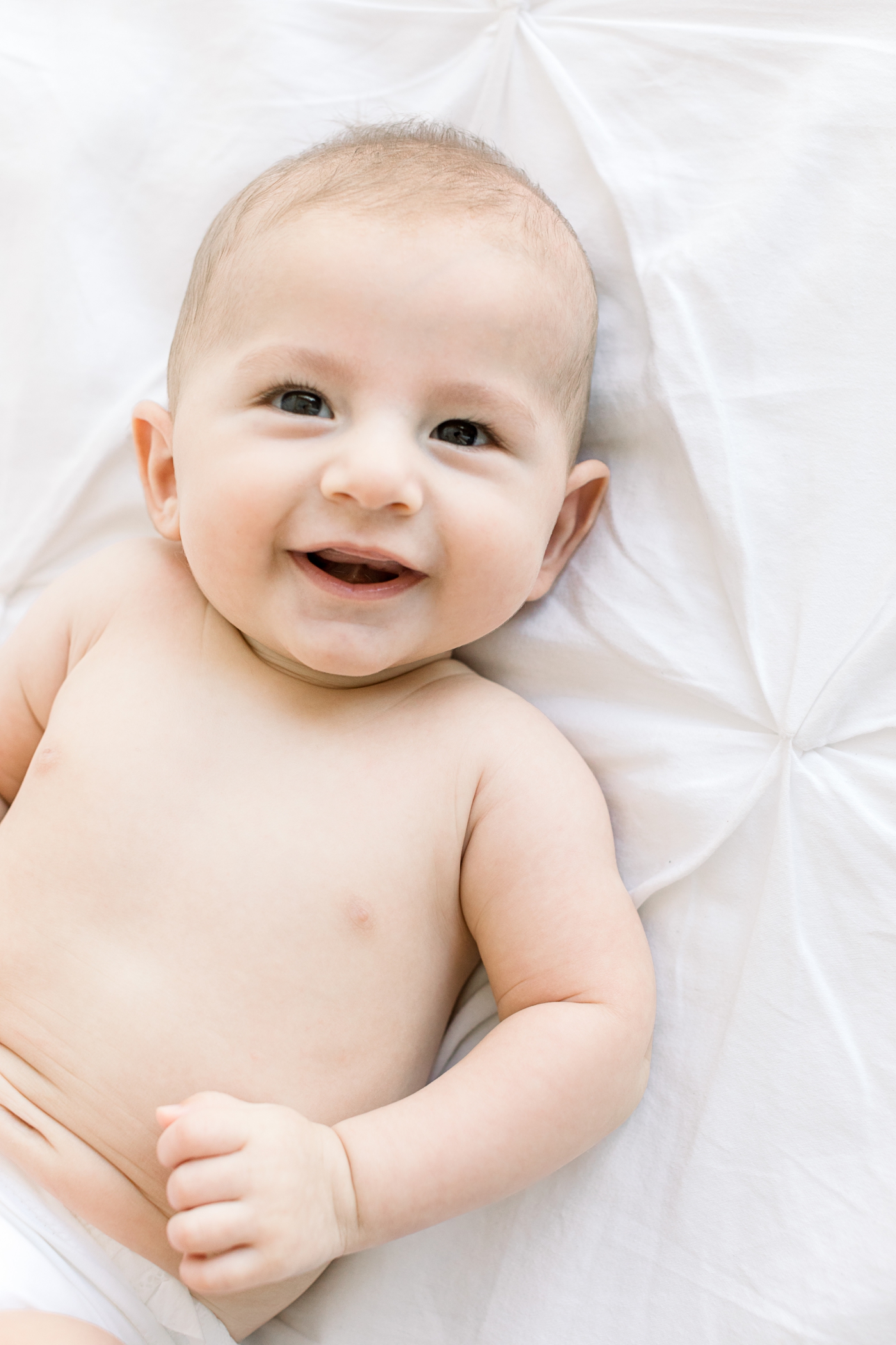 Baby boy smiling on bed during family photoshoot in Austin studio. Photo by Sana Ahmed Photography.