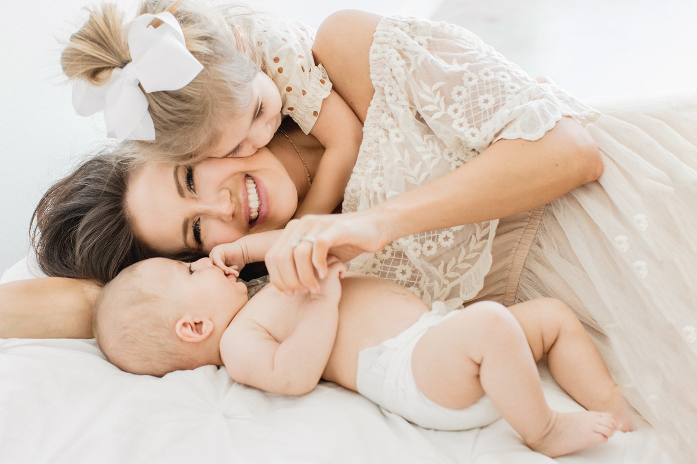 Mom smiles as she cuddles on studio bed with little children during lifestyle family session. Photo by Austin family Photographer, Sana Ahmed Photography.
