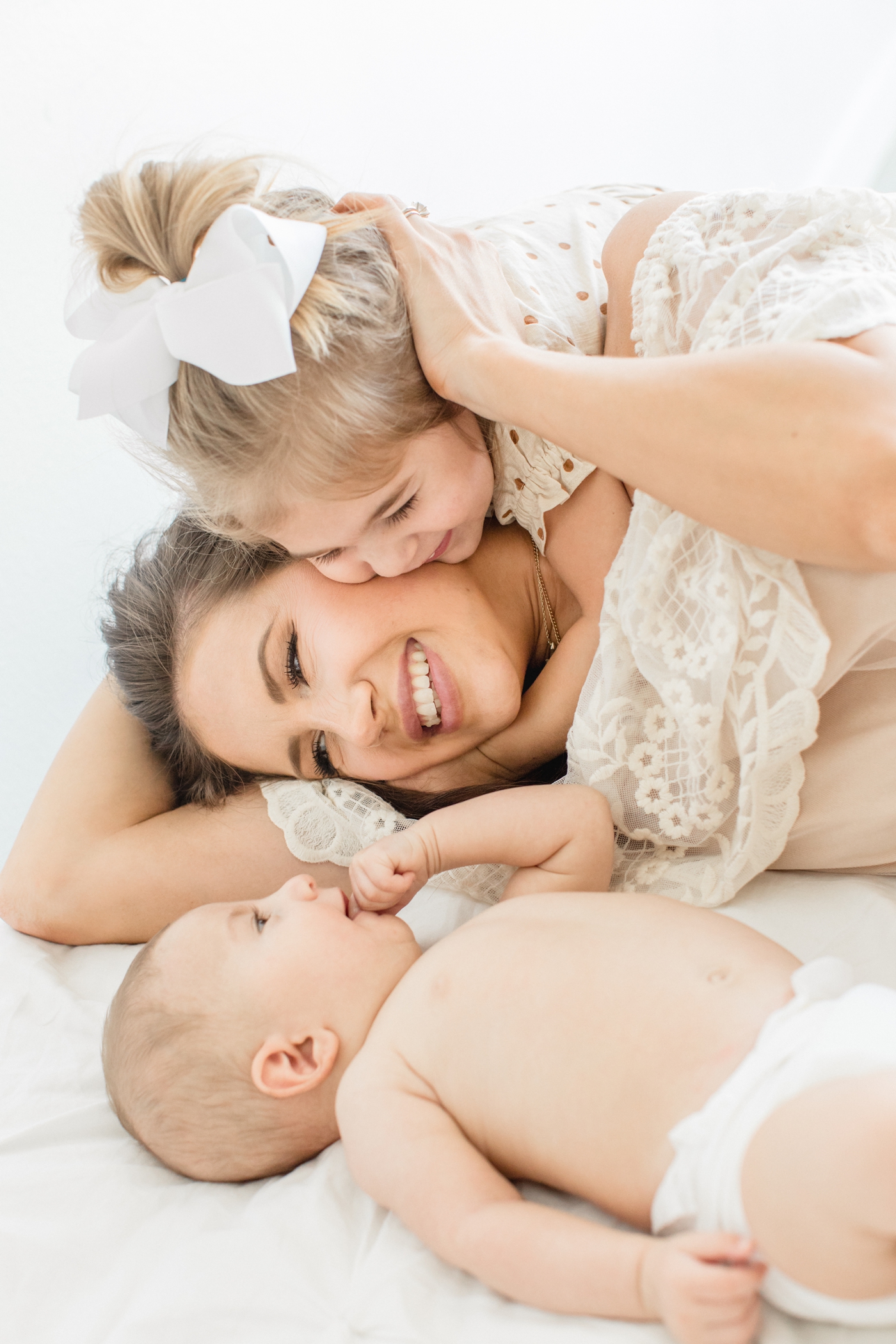 Mom being cuddled by little girl while baby watches them play. Photo by Austin lifestyle family photographer, Sana Ahmed Photography.