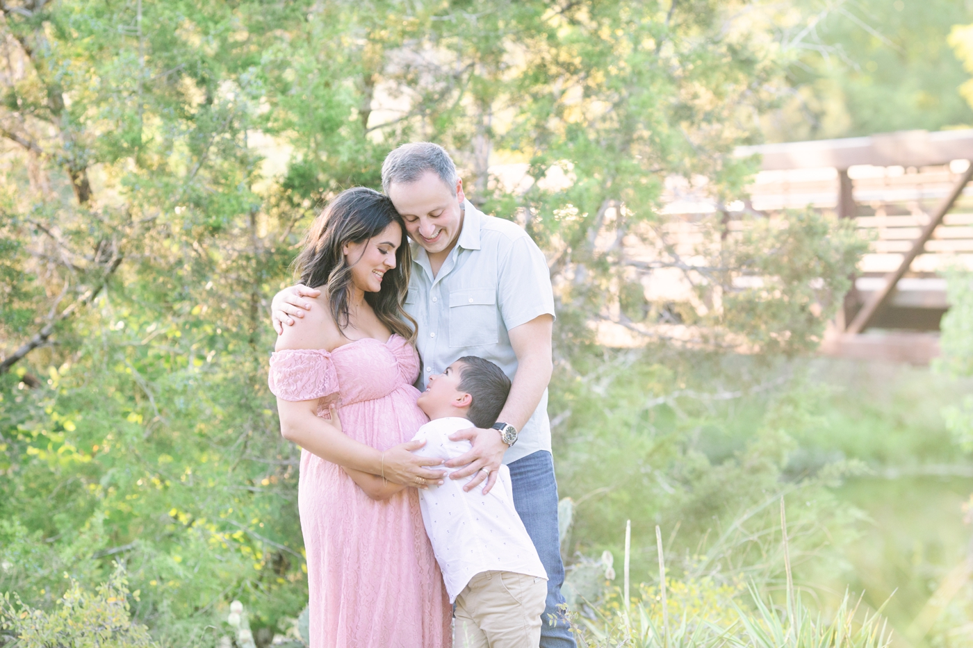 Family of three hugging during park maternity session in Austin TX. Photo by Sana Ahmed Photography.