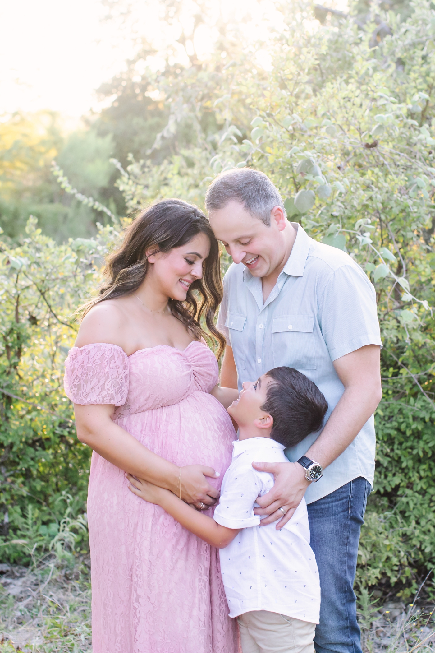 Sunlit portrait of family smiling at each other during maternity session. Photo by Sana Ahmed Photography.