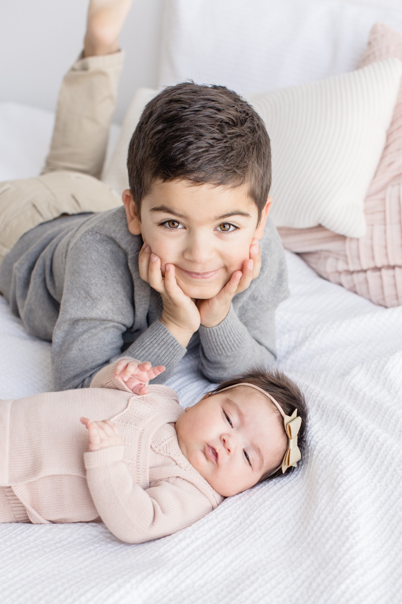 Big brother posing with baby sister on bed. Photo by Sana Ahmed Photography.