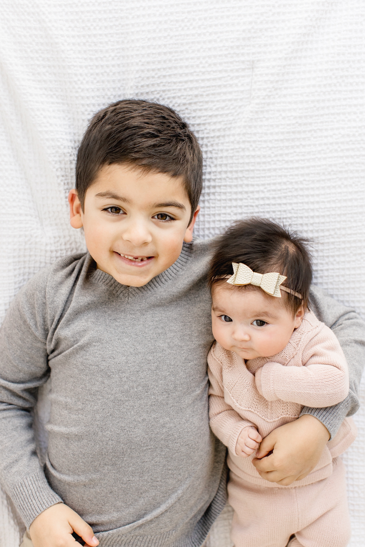 Big brother smiling with baby sister in his arms. Photo by Sana Ahmed Photography.