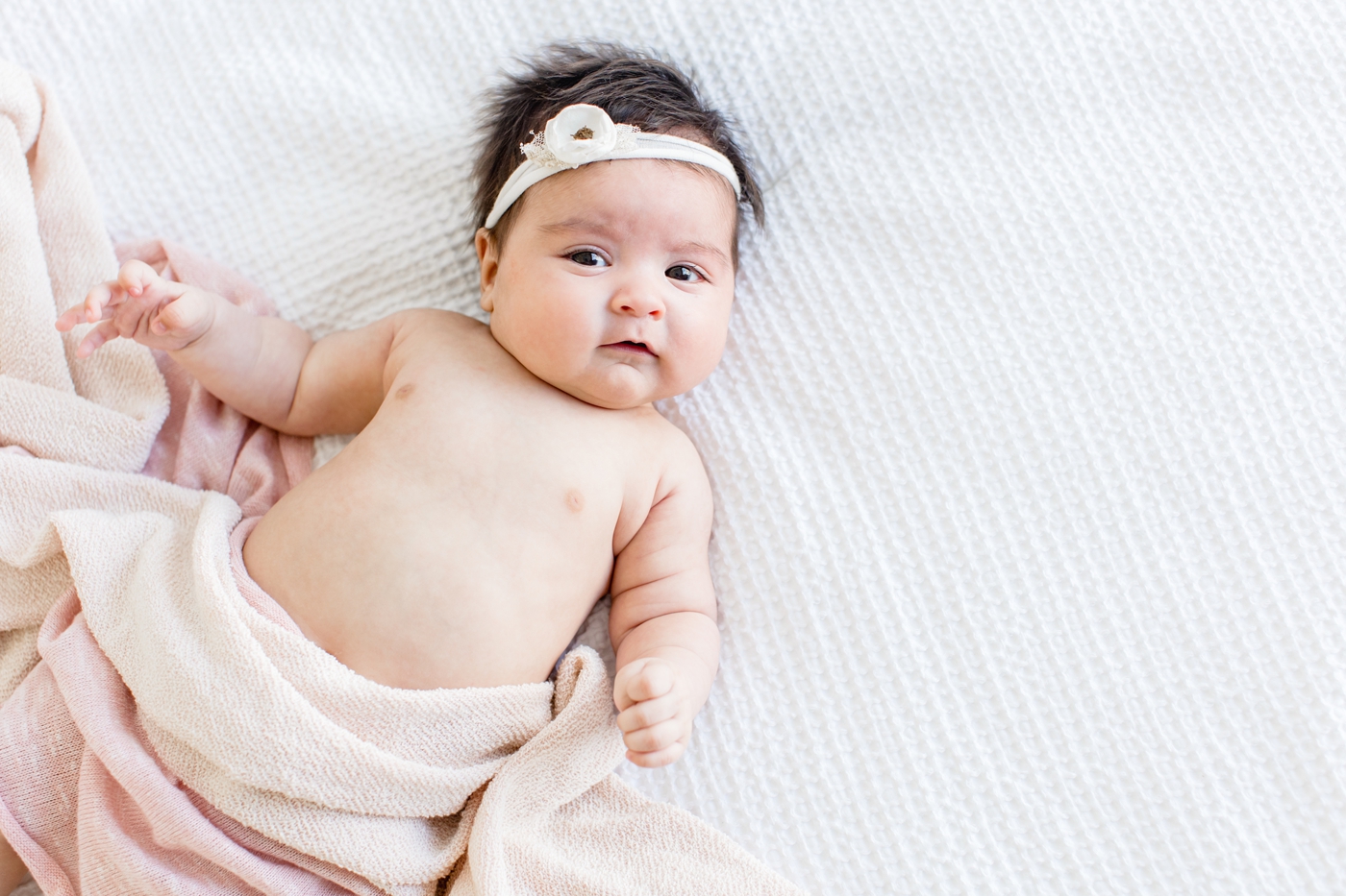 Photo of baby looking at camera with pink knit swaddle by Sana Ahmed Photography.